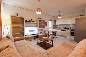 A modern living room with a sofa, coffee table, and TV. There is a dining area with chairs and a kitchen in the background. - Sanpietro Vacation Apartment 048 (Ishëm)