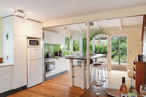 A modern kitchen with white cabinets, a microwave, and a sink. There is a wooden dining table with chairs and a bar stool. - Birdsong at Bawley - Beach Escape (Bawley Point)