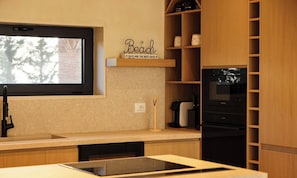 A modern kitchen with a built-in oven, a window, and a shelf with a 'Beach' sign.