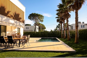 A modern outdoor pool area with a dining set and palm trees.