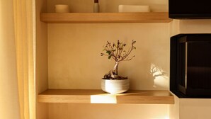 Una habitación minimalista con un estante de madera que sostiene un bonsái, un pequeño jarrón y una vela.