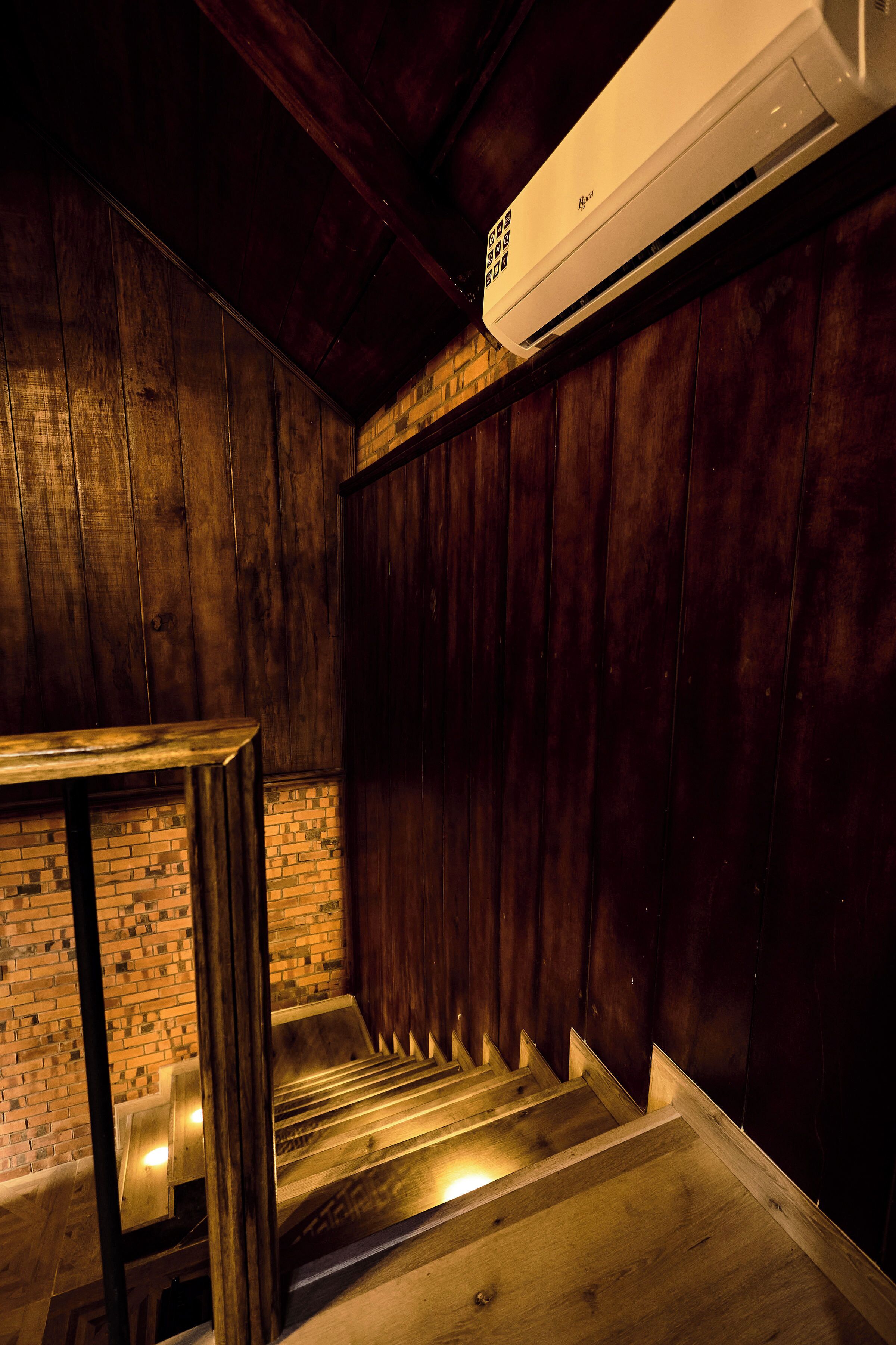 A room with wooden walls, a brick wall section, and a staircase with a metal railing.