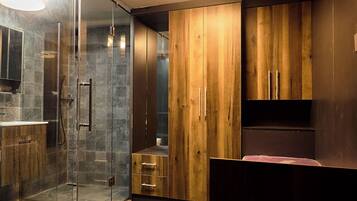 A modern bathroom with a glass shower enclosure, wooden cabinets, and a herringbone-patterned floor.