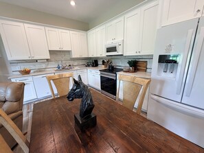 A modern kitchen with white cabinets, a wooden dining table, and a horse sculpture centerpiece.