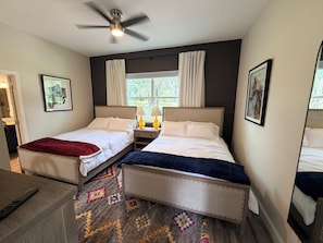 A hotel room with two beds, a ceiling fan, a window with curtains, and a carpeted floor.