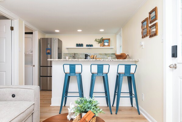 Una cocina moderna con una isla central, tres taburetes azules y un refrigerador.