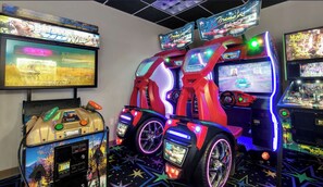 Eine Spielhalle mit mehreren Rennspielautomaten, darunter ein markanter Rennspielautomat in Rot und Blau mit Lenkrad und großem Bildschirm.