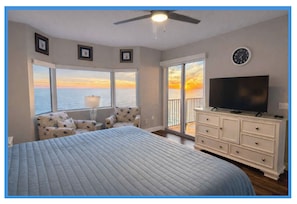 A bedroom with a large bed, a television, a dresser, and a view of the ocean at sunset. - 3pm Check In Beachfront 2 Bedroom K/Q/Q+SleeperSofa 2RECLINERS Gulf front Master (Panama City Beach)