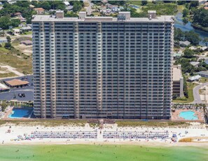 Ein Hochhaus-Hotel mit mehreren Stockwerken, einem Pool und einem Strandbereich mit Sonnenschirmen und Personen.