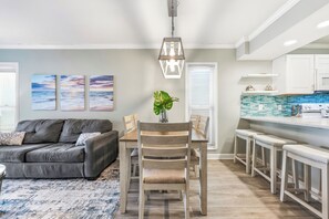 A modern kitchen with white cabinets, a blue backsplash, and a dining area with a wooden table and chairs. - 2BD/2BA Oceanfront Corner Unit-Pet Friendly- Windy Shores 306 (North Myrtle Beach)
