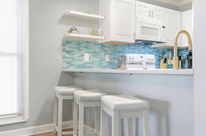 A kitchen with white cabinets, a blue-tiled backsplash, a white countertop, and three white stools. - 2BD/2BA Oceanfront Corner Unit-Pet Friendly- Windy Shores 306 (North Myrtle Beach)