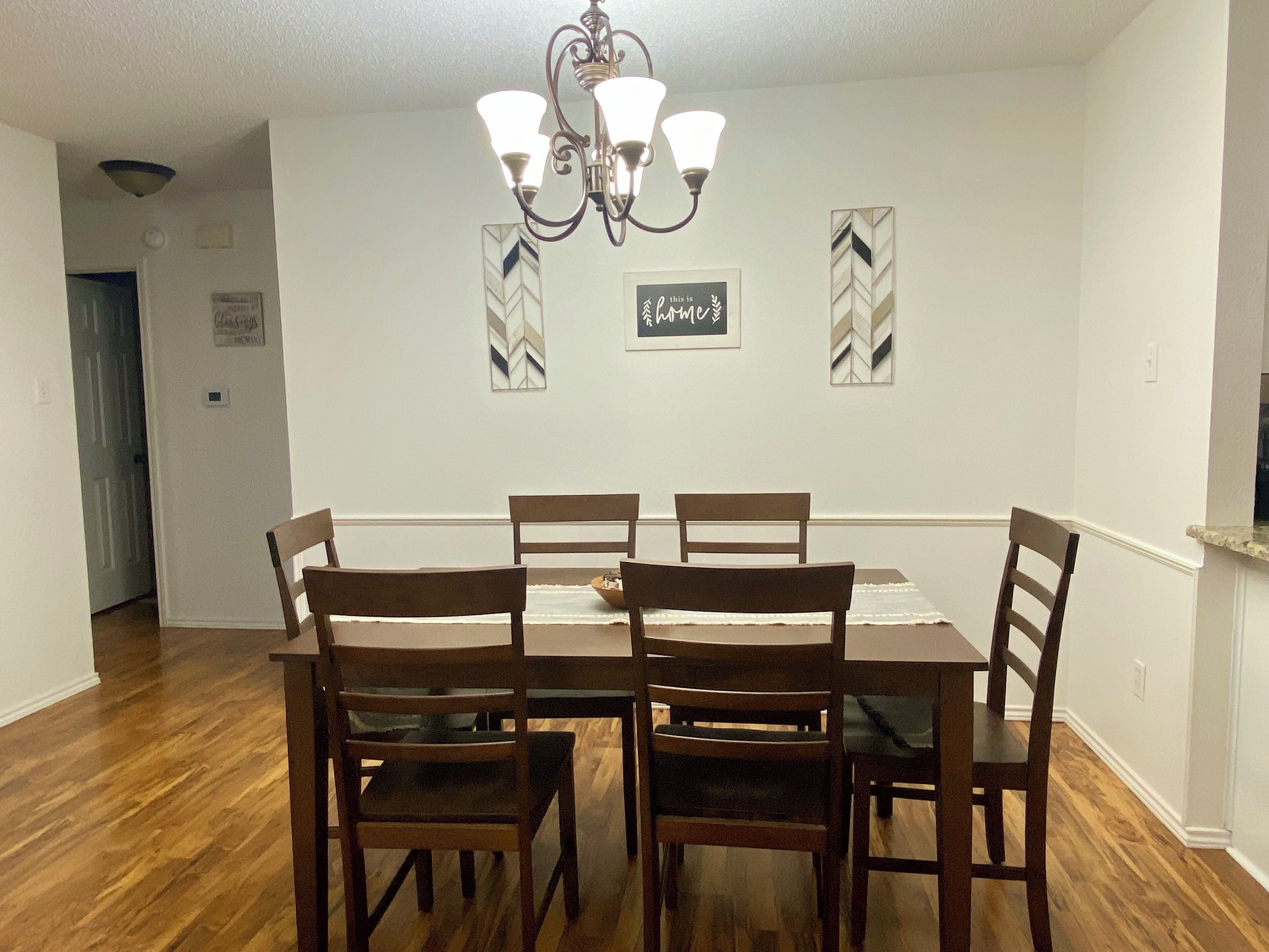 Un comedor con una mesa rectangular, cuatro sillas de madera, una araña y dos espejos decorativos colgados en la pared.