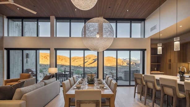 A spacious dining area with a large table set for six, a sofa, and a kitchen area with wooden cabinets and pendant lighting. - Luxury Moab Casita with Resort Pool, Hot Tub & Bunk Room (Moab)