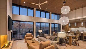 A spacious living area with a large window overlooking a mountainous landscape, a ceiling fan, and a modern kitchen with wooden cabinets and pendant lighting. - Luxury Moab Casita with Resort Pool, Hot Tub & Bunk Room (Moab)