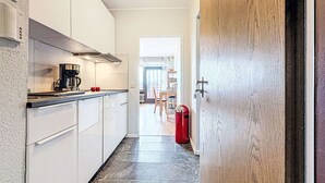 Kapea keittiö, jossa on valkoiset kaapit, musta työtaso ja kahvinkeitin.