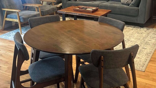 Una sala de estar moderna con un panel de pared de madera, un sofá gris, una mesa de centro redonda de madera y sillas a juego.