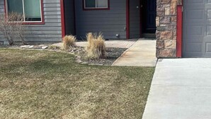 Una casa residencial con fachada de piedra, techo rojo y un patio delantero con entrada de hormigón.