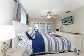A bedroom with a bed, nightstand, lamp, ceiling fan, and a view of the outside. - Private Beach Access, Gorgeous Partial Views (Indian Shores)