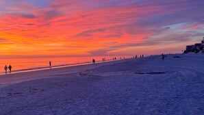 Una playa con gente caminando y un atardecer al fondo.