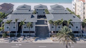 Un hotel frente a la playa con edificios de varios pisos, una escalera central y palmeras.