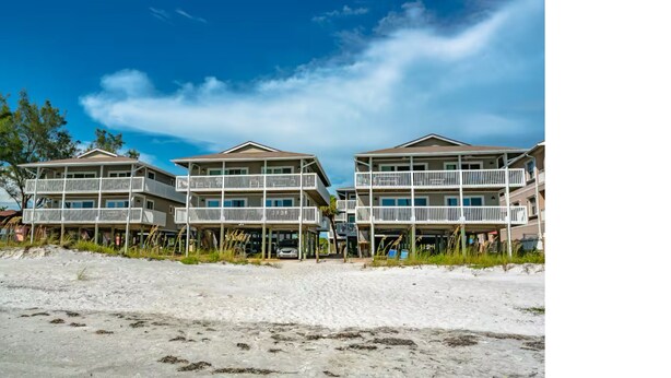 Un hotel frente a la playa con varios balcones y una playa arenosa al frente.