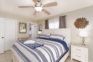 Ein Schlafzimmer mit einem Bett, einem Nachttisch, einem Deckenventilator und einer Wanddekoration.