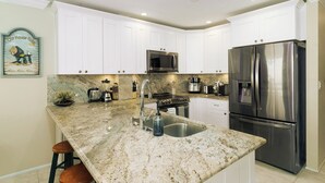 Una cocina con armarios blancos, un refrigerador de acero inoxidable, un microondas y una encimera de granito.