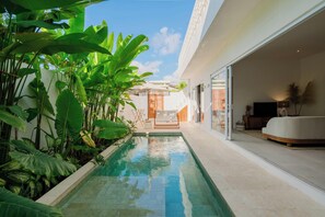 A pool with tropical plants, a white sofa, and a TV in a modern room. - Lumi Villa by Betterplace (Pecatu)