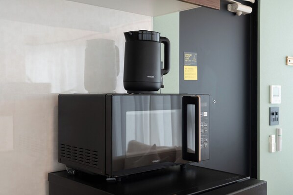 A black Yamazen coffee maker on a black countertop, a wall-mounted security camera, and a door with a light switch and a smoke detector. - ORI Ikebukuro (Tokyo)
