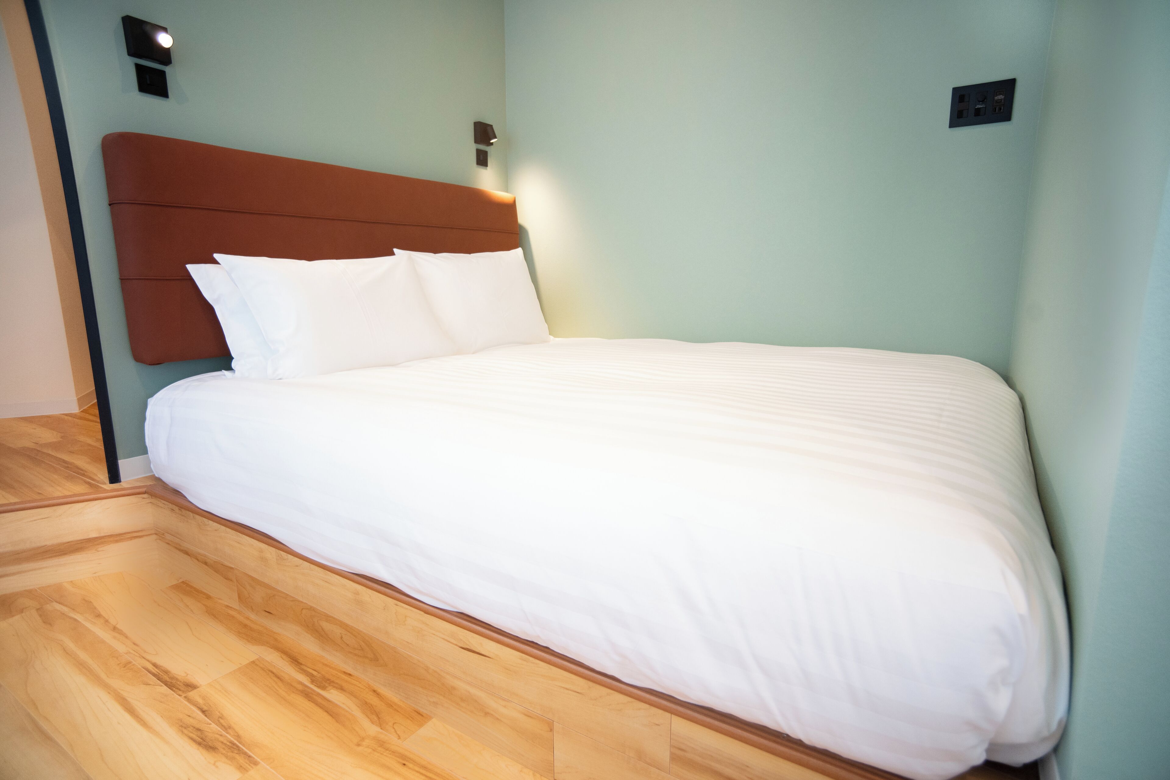 A neatly made bed with white linens, a wooden headboard, and a light-colored wall.
