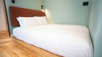 A neatly made bed with white linens, a wooden headboard, and a light-colored wall.