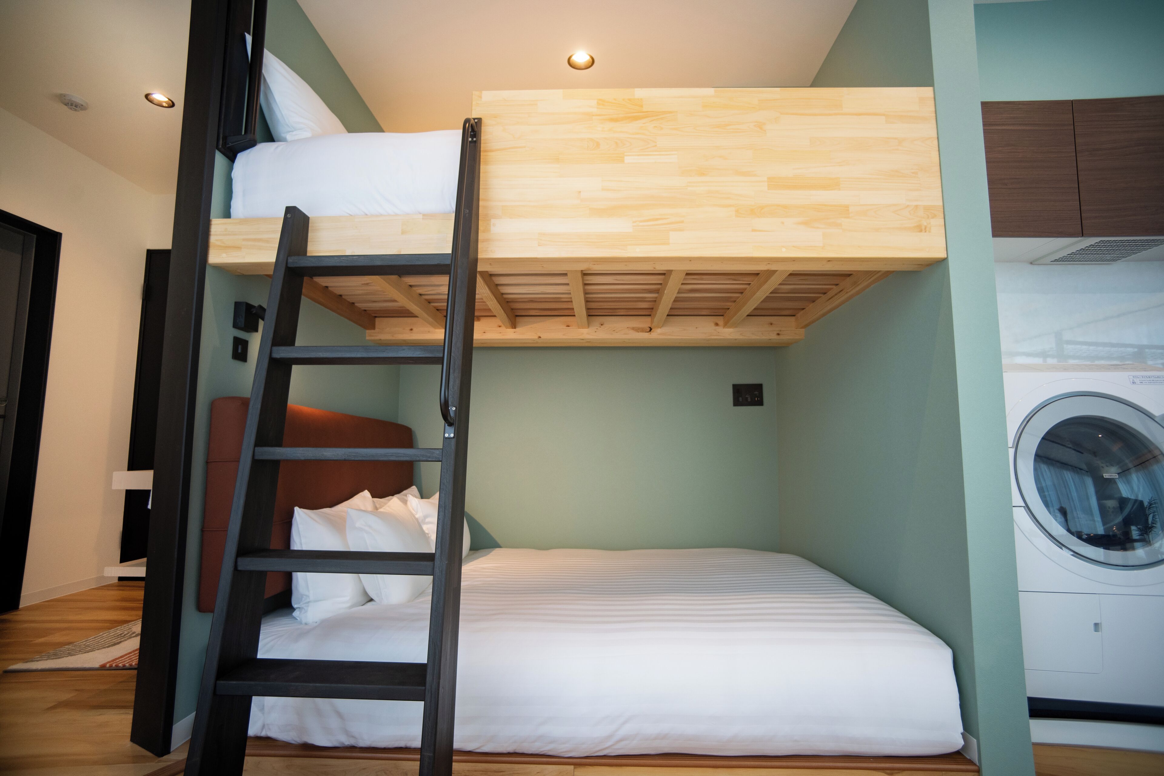 Habitación con literas, una escalera de madera, lavadora y pared verde claro.