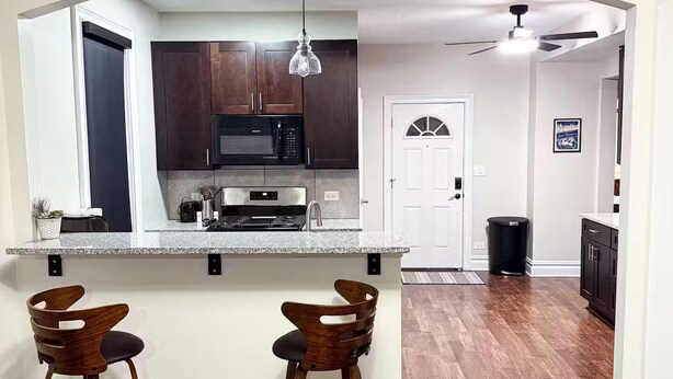 A modern kitchen with dark wooden cabinets, a granite countertop, and two bar stools. - Spacious 6 bed 2 bath suburban escape 20 min from downtown Chicago (Blue Island)
