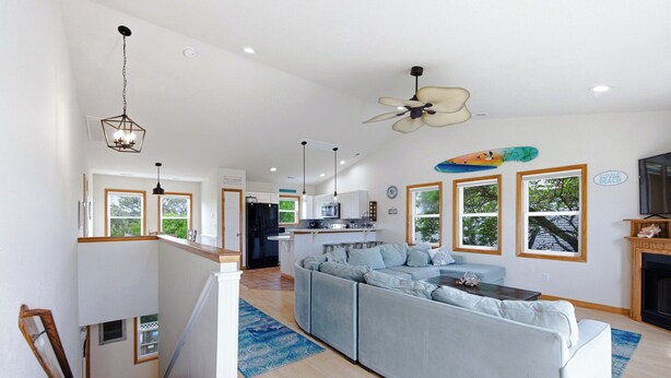 Een moderne keuken met een centraal eiland, een zithoek met een grote grijze bank, en een trap naar een hoger gelegen verdieping.