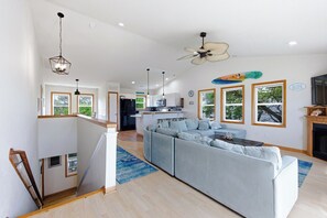 Eine moderne Küche mit einer zentralen Kochinsel, ein Essbereich mit einem großen grauen Sofa und eine Treppe, die in einen oberen Bereich führt.