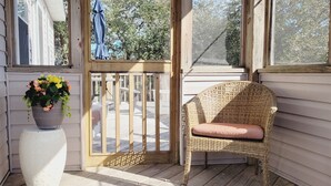 Een veranda met een rieten stoel, een bloempot en een houten leuning.