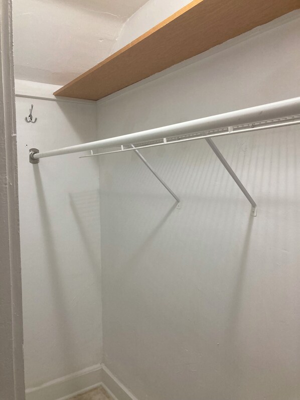 A walk-in closet with a metal rod rack and a wooden shelf above.