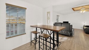 Een moderne woonkamer met een houten eettafel, twee barkrukken, een grijze bank en een plafondventilator.