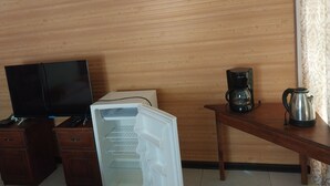 A room with a wooden wall, a television on a wooden cabinet, a coffee maker, and a kettle on a wooden table.