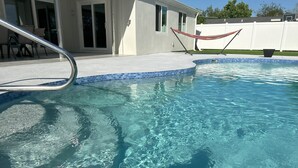 A clear swimming pool with a metal ladder, a white fence, and a hammock in the background. - Newly Renovated, Modern, Pristine w/ Heated Pool - 10 min to Siesta Beach (Sarasota)