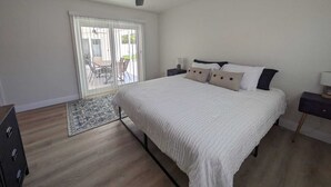 A bedroom with a bed, a ceiling fan, a nightstand, a dresser, and a view of an outdoor patio. - Newly Renovated, Modern, Pristine w/ Heated Pool - 10 min to Siesta Beach (Sarasota)