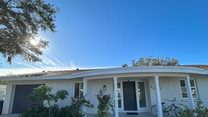 A single-story house with a curved roof, a front porch with white columns, and a front door. There are potted plants in front of the house and a bicycle parked to the right. - Newly Renovated, Modern, Pristine w/ Heated Pool - 10 min to Siesta Beach (Sarasota)