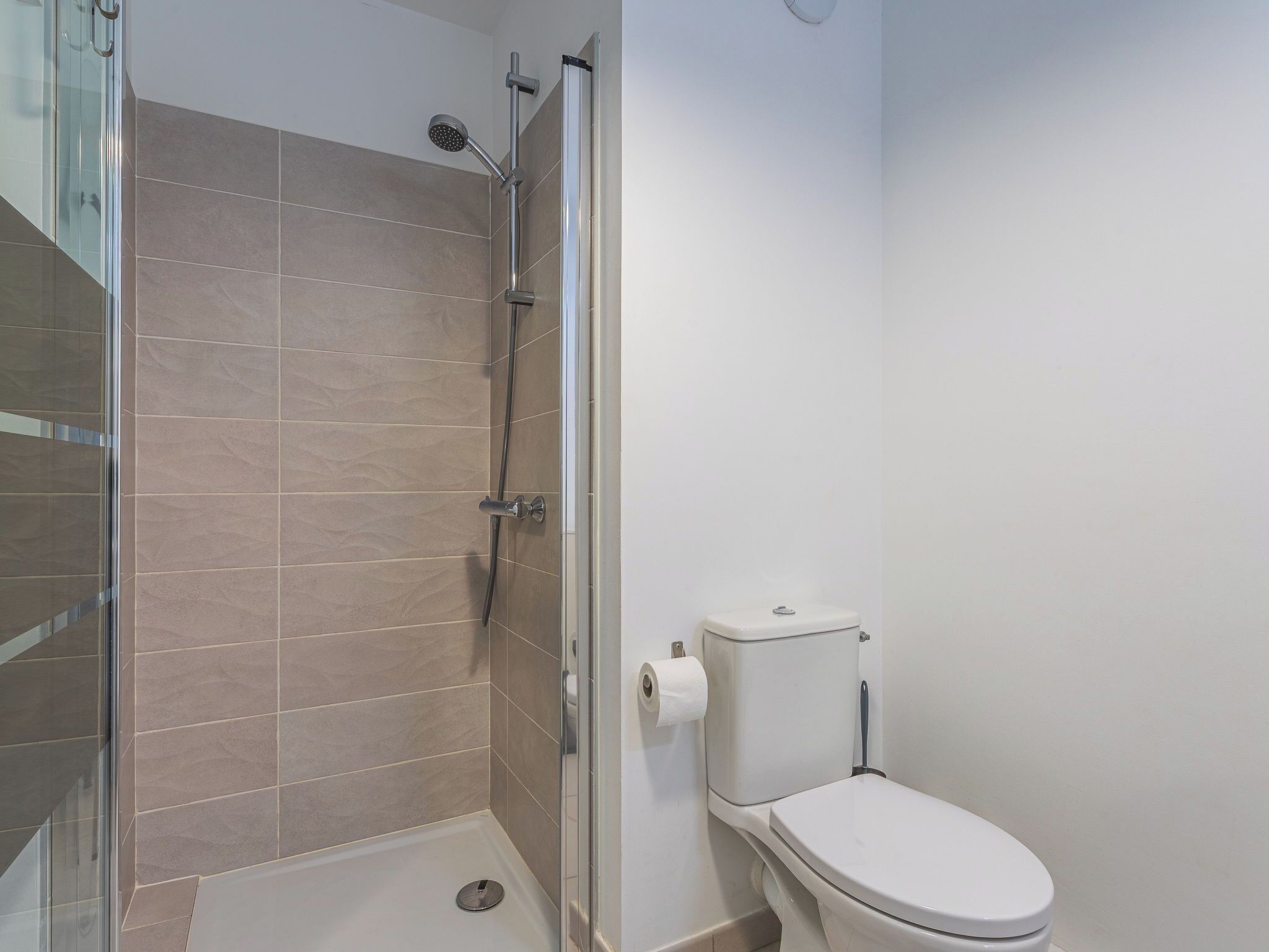 Een badkamer met een douchecabine van glas, een toilet en een rol toiletpapier aan de wand.