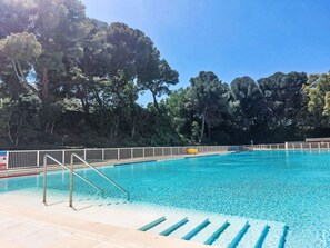 Une piscine avec des marches permettant d’y accéder, entourée d’arbres.