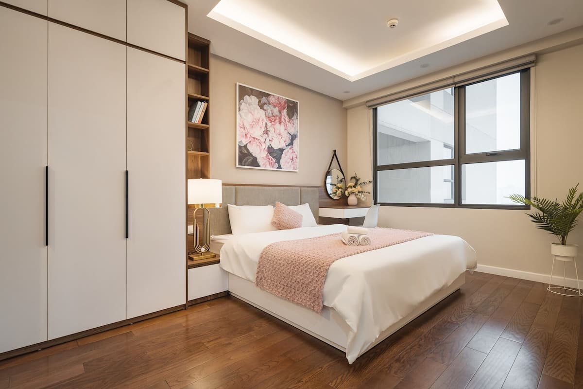 A bedroom with a bed, bedside table, lamp, and a large window.