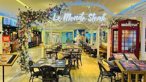 A restaurant interior with tables, chairs, a sign reading 'Le Monde Steak,' and a telephone booth. - Hopo Apt - Vinhomes D'capitale Luxury (Hanoi)