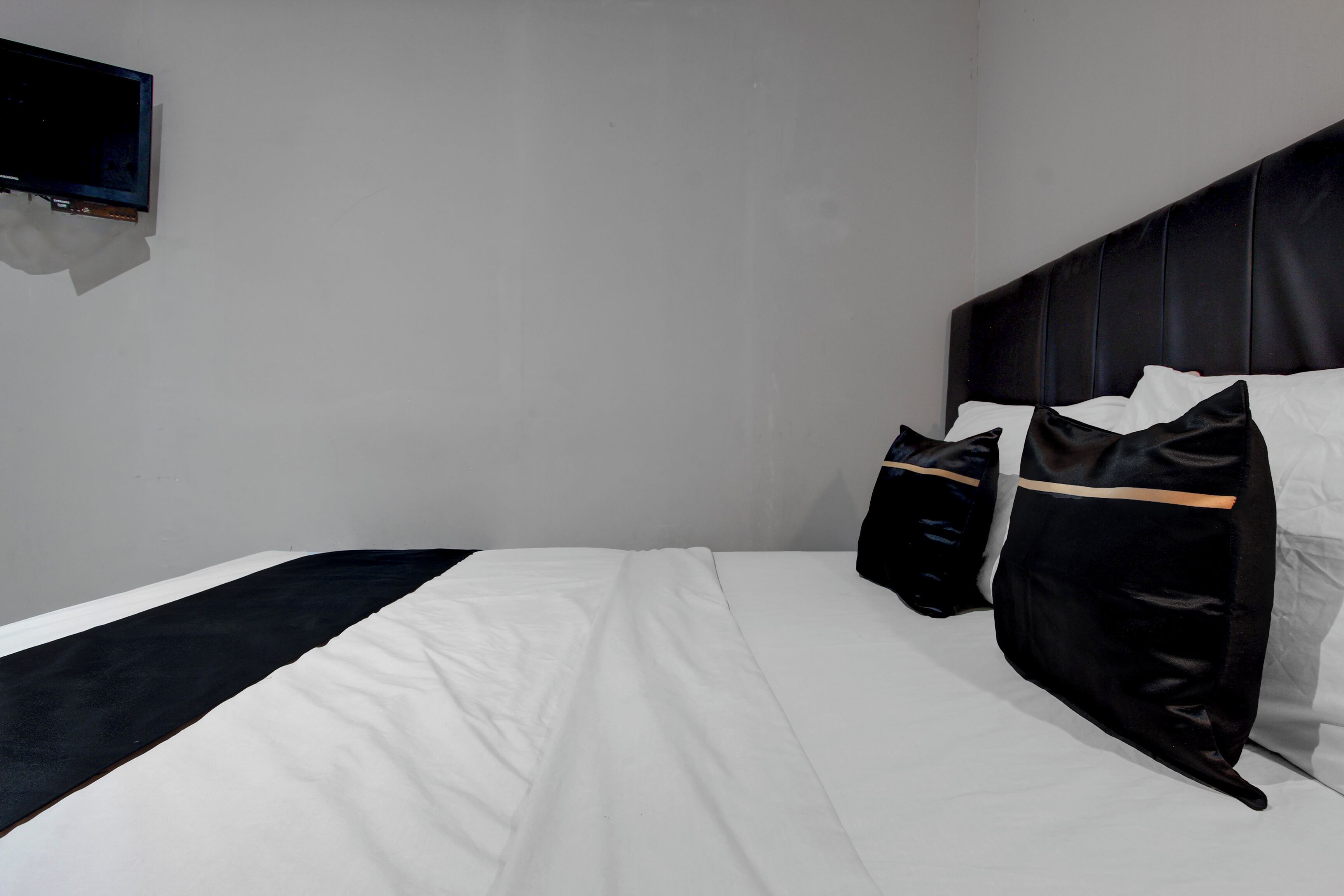 Habitación de hotel con cama, almohadas, un televisor de pantalla plana montado en la pared y cabecero.