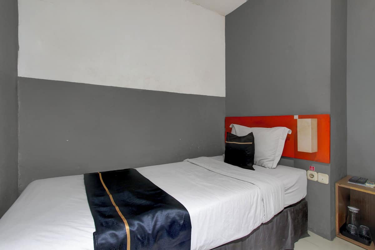 A single bed with a white mattress, a dark blue blanket, and a red headboard.