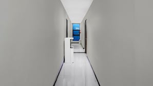 Un couloir étroit aux murs blancs, avec une porte bleue au fond, qui mène à une pièce dont un des murs est bleu.