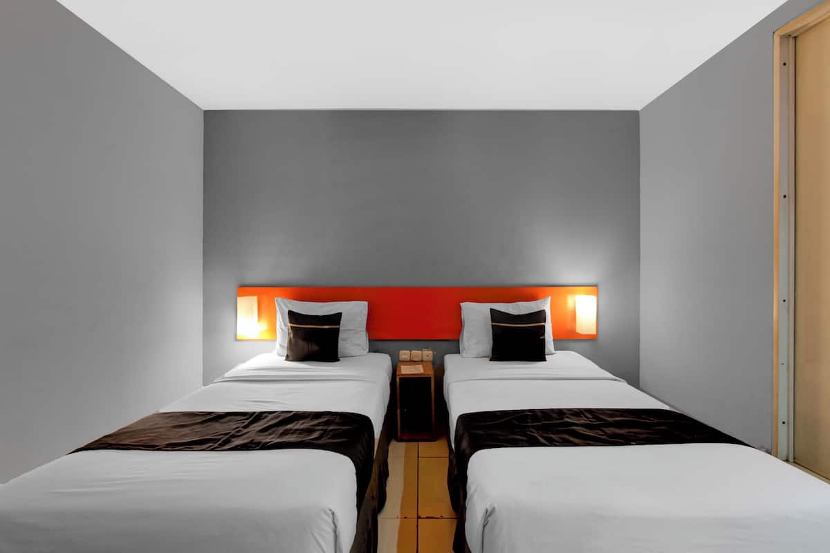A hotel room with two beds, a red accent wall, and a wooden door.